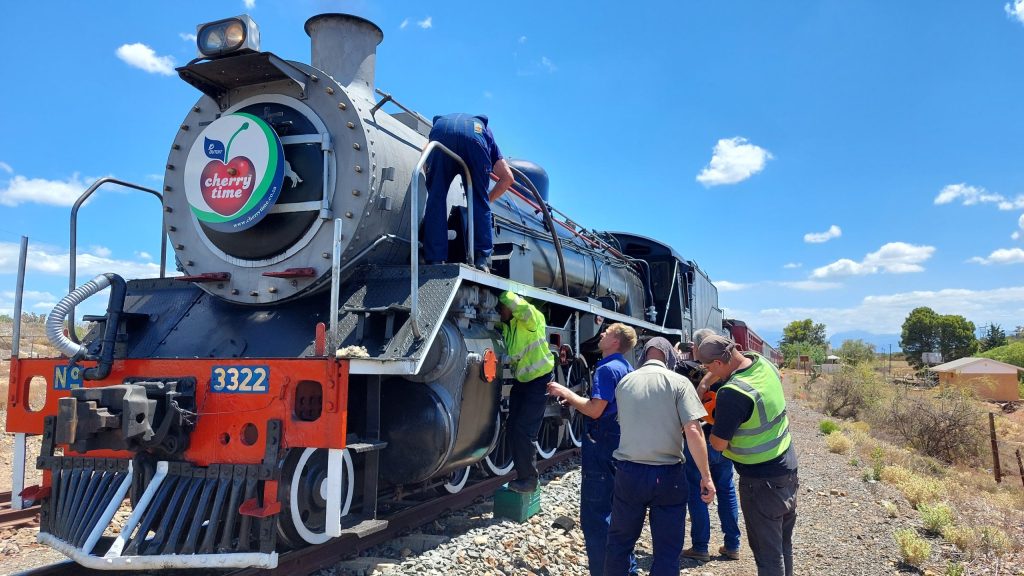 Group of people working on a vintage steam locomotive outdoors.