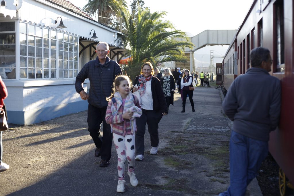 People walking beside a train station platform with a train on the right.