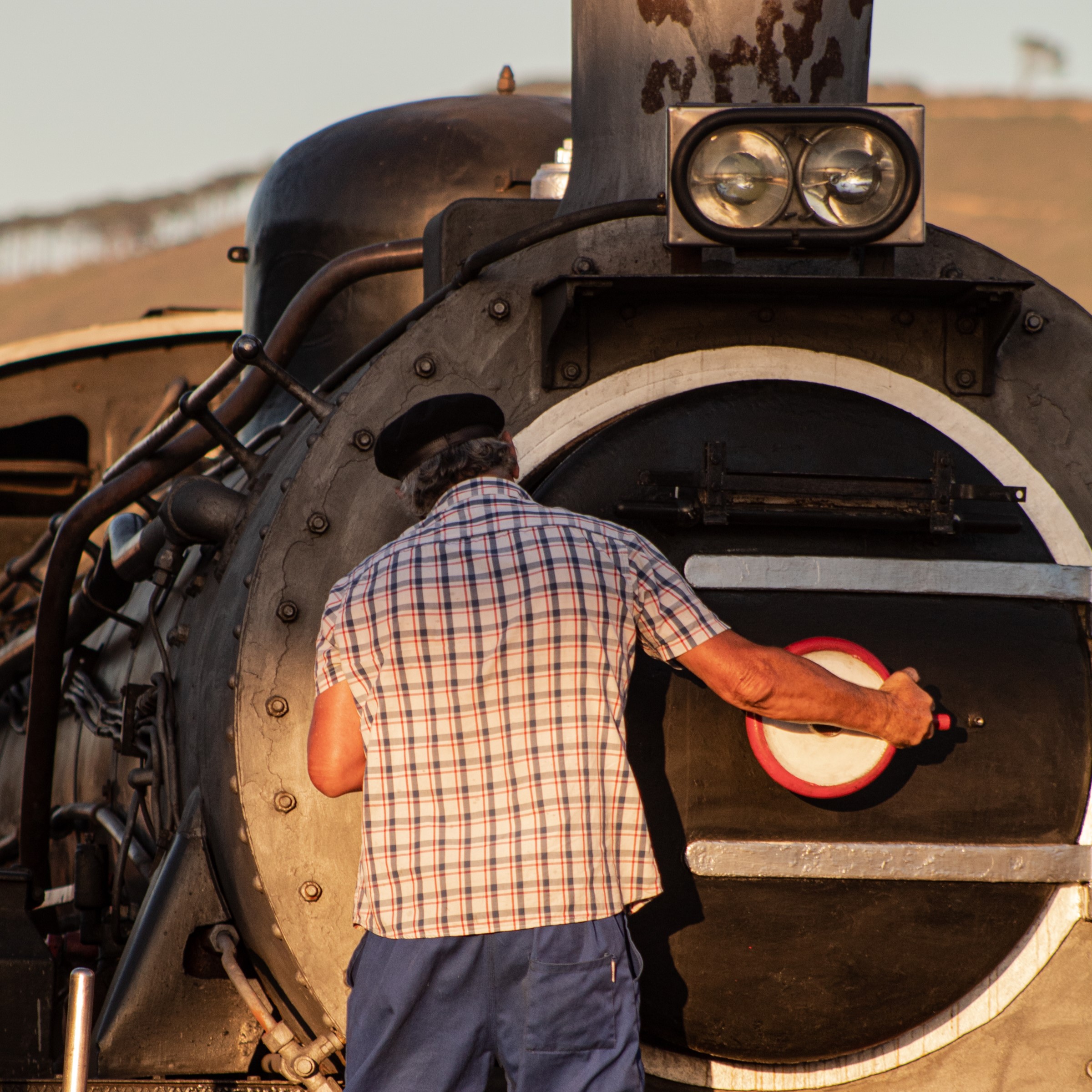 Person in checkered shirt inspecting the front of a steam locomotive.