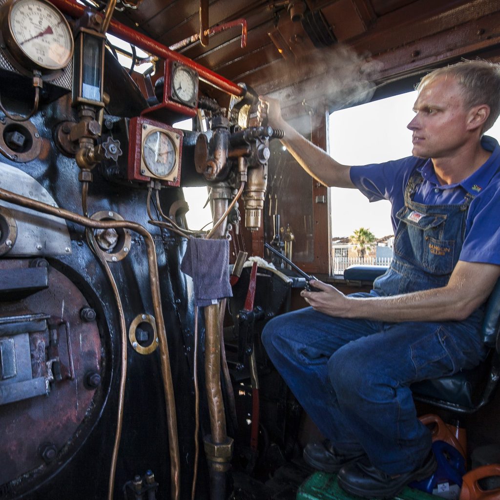 Man operating steam train controls in vintage locomotive cabin.
