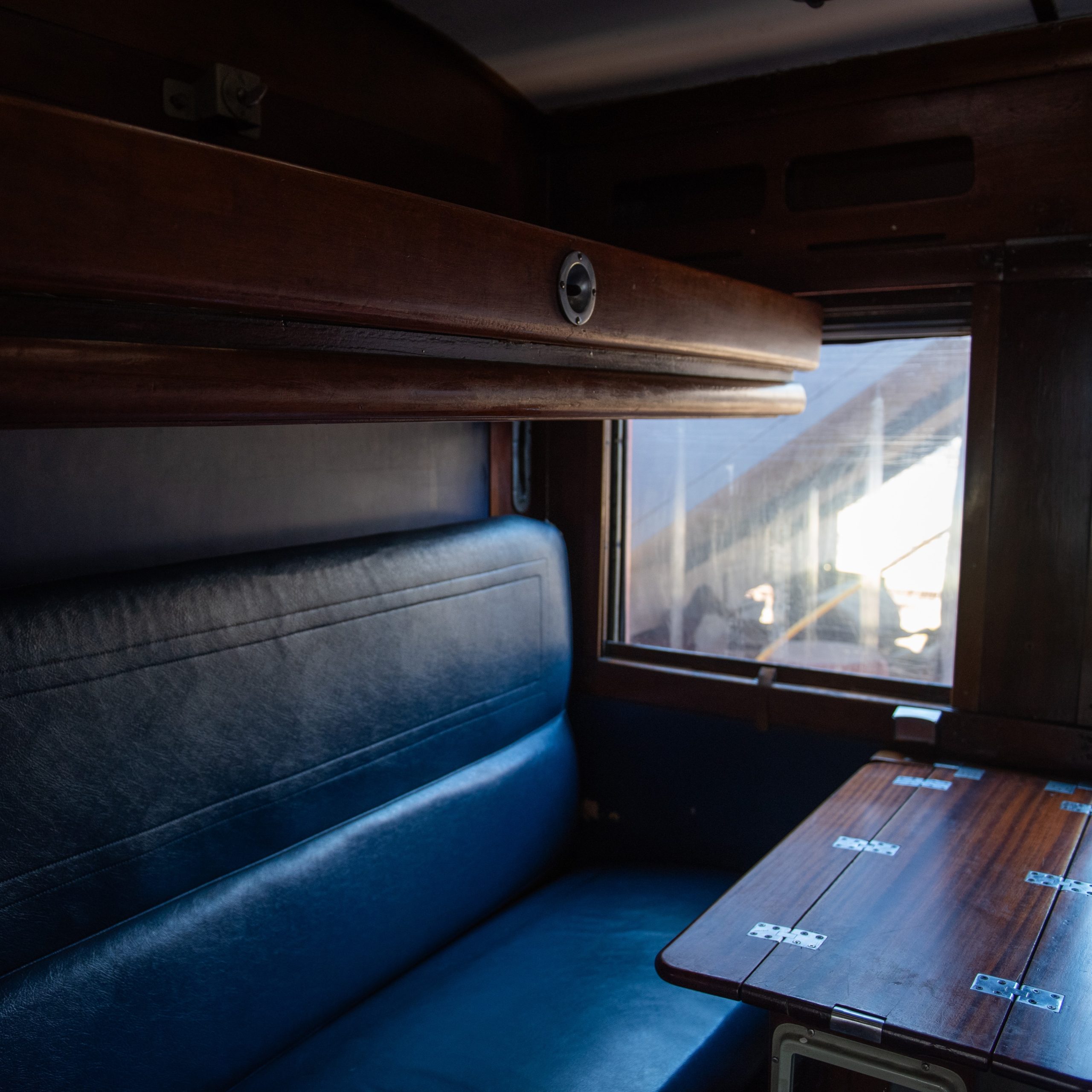 Vintage train cabin with blue seat and wooden interior.